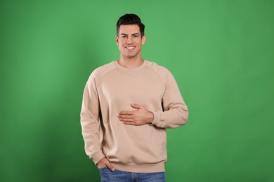 Happy healthy man touching his belly on green background
