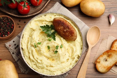 Photo of Bowl of tasty mashed potatoes with parsley, black pepper and cutlet served on wooden table, flat lay