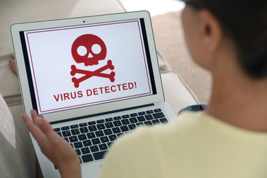 Woman using laptop with warning about virus attack on screen at home, closeup