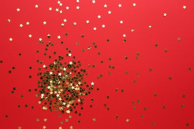 Gold confetti stars on red background, flat lay. Christmas celebration