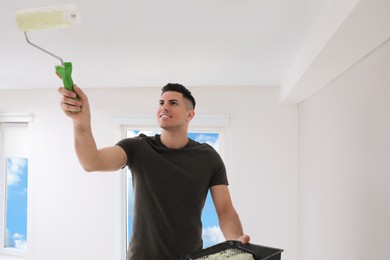 Photo of Man painting ceiling with roller in room. Space for text
