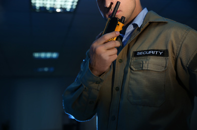 Professional security guard with portable radio set in dark room, closeup