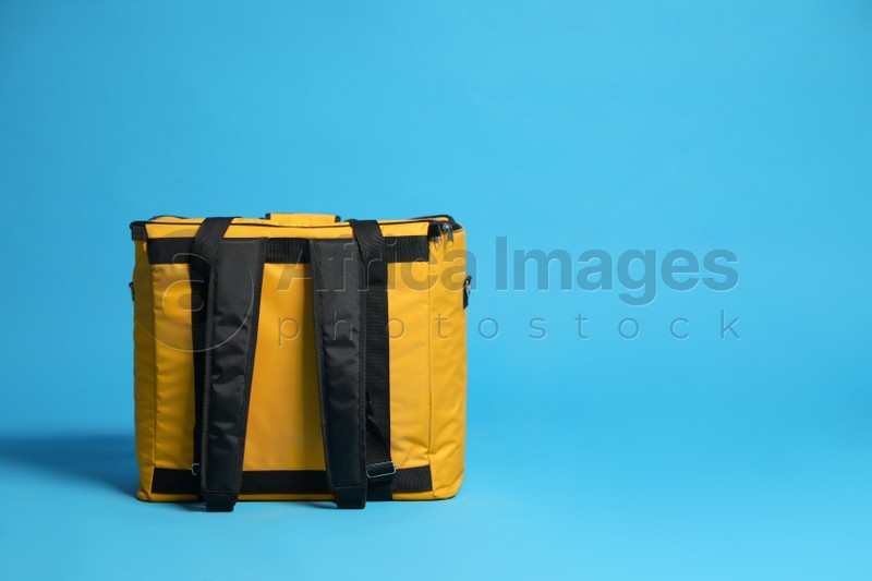 Modern yellow thermo bag on light blue background. Space for text