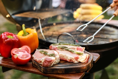 Board with raw meat and vegetables near barbecue grill outdoors