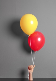 Wooden hand holding colorful balloons on gray background