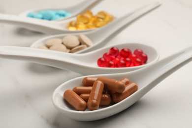 Photo of Spoons with different dietary supplements on white table, closeup