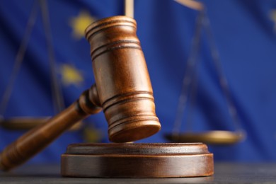 Wooden judge's gavel and Scales of justice on grey table against European Union flag, closeup