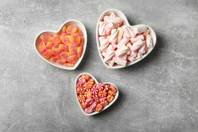 Tasty sweets in heart shaped bowls on grey table, flat lay
