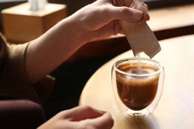 Woman adding sugar to aromatic coffee at table in cafe, closeup