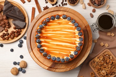 Photo of Delicious cheesecake with caramel and blueberries on white wooden table, flat lay