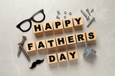 Photo of Cubes with phrase Happy Father's Day, paper glasses, mustache, screws and gift box on light background, flat lay
