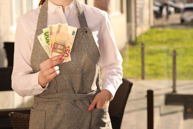 Photo of Waitress holding payment for order and tips at outdoor cafe, closeup