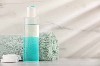 Bottle of micellar water, towel and cotton pads on white table against marble background, space for text