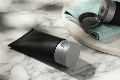 Men's cosmetic products in black tubes and towel on white marble table, closeup