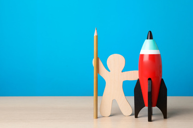 Bright toy rocket, human model and pencil on white wooden desk. Space for text