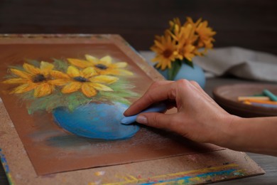 Woman drawing beautiful flowers in vase on paper with pastel at table, closeup
