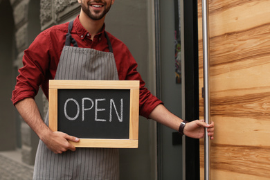 Young male business owner holding OPEN sign near his cafe, closeup