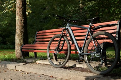 Modern bicycle near wooden bench outdoors, space for text