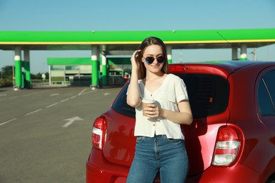 Beautiful young woman with coffee near car at gas station