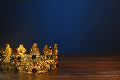 Photo of Beautiful golden crown with gems on wooden table, space for text. Fantasy item