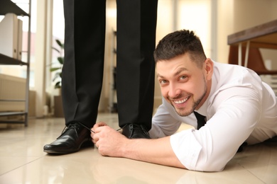 Man tying shoe laces of his colleague together in office, closeup. Funny joke