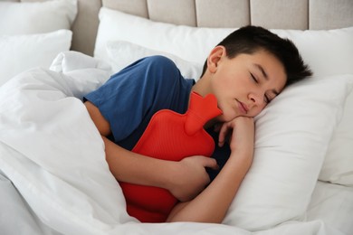 Sick teenage boy with hot water bottle sleeping in bed at home