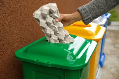 Photo of Woman throwing carton egg box into recycling bin outdoors, closeup