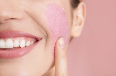 Young woman applying natural scrub on her face against color background, closeup