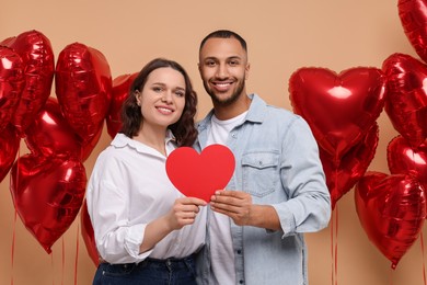Photo of Lovely couple with red paper heart on beige background. Valentine's day celebration