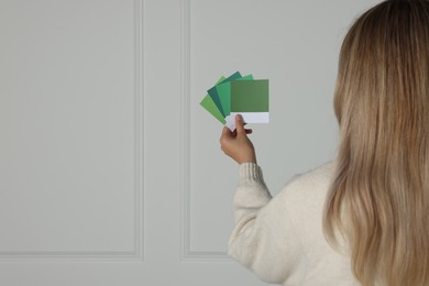Photo of Woman choosing paint shade for wall indoors, focus on hand with color sample cards. Interior design