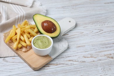 Serving board with french fries, guacamole dip and avocado on white wooden table, space for text