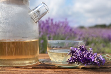 Tasty herbal tea and fresh lavender flowers on wooden table in field, closeup