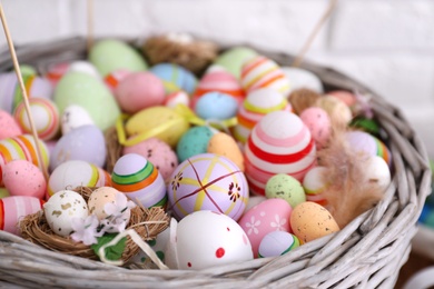 Many different Easter eggs in wicker basket on light background, closeup