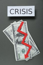 Paper sheet with word Crisis, money and descending red arrow on grey background, flat lay