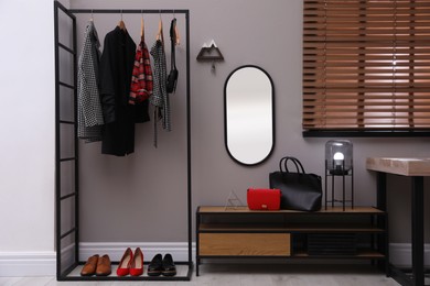 Modern hallway interior with stylish furniture, mirror and wooden hanger for keys on grey wall