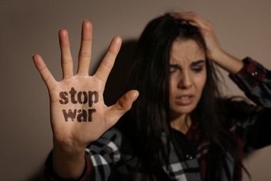 Upset young woman showing palm with phrase Stop War near beige wall, focus on hand