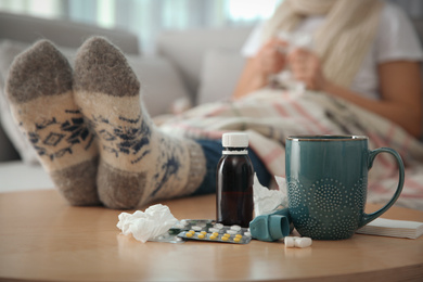 Person in warm socks near table with different remedies indoors, closeup. Influenza virus
