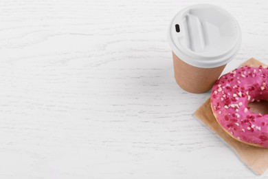 Tasty frosted donut and hot drink on white wooden table, space for text