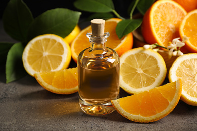 Bottle of essential oil and citrus fruits on grey table