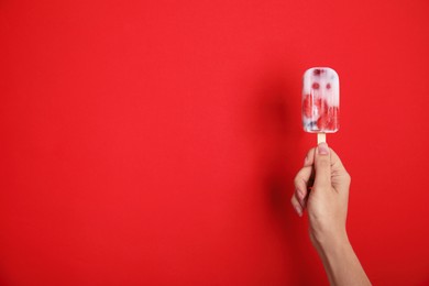 Woman holding berry popsicle on red background, closeup. Space for text