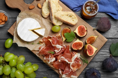 Photo of Board with delicious figs, proscuitto, cheese and grapes on grey wooden table, flat lay