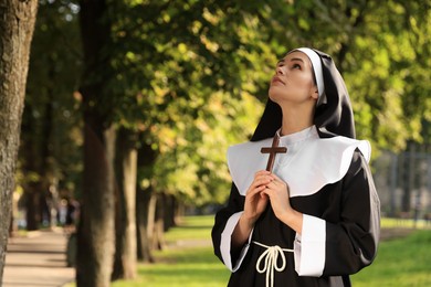 Young nun with Christian cross in park on sunny day, space for text
