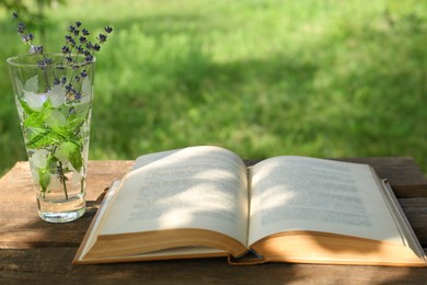 Open book with flowers in glass on wooden table outdoors