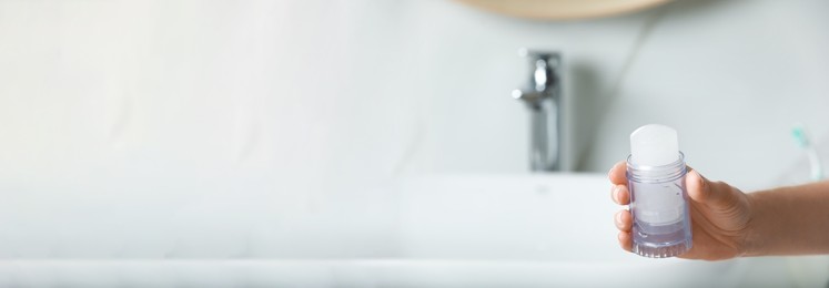 Woman holding crystal alum deodorant in bathroom, closeup view with space for text. Banner design