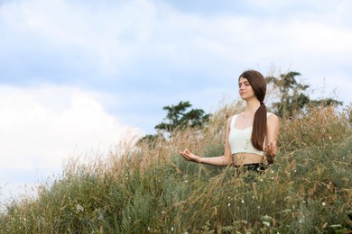 Teenage girl meditating on hill. Space for text