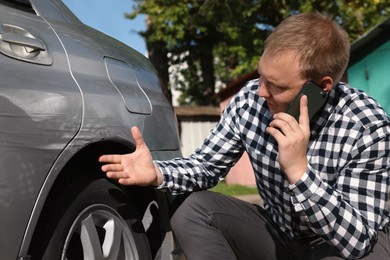 Man talking on phone near car with scratch outdoors