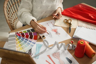 Fashion designer creating new clothes in sketchbook at wooden table indoors, closeup