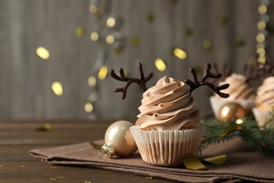 Tasty Christmas cupcake with chocolate reindeer antlers on wooden table. Space for text