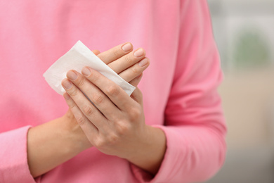 Woman cleaning hands with paper tissue on blurred background, closeup
