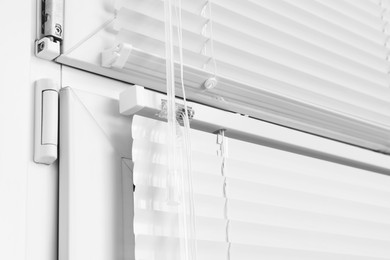 Window with closed white horizontal blinds and control system indoors, closeup